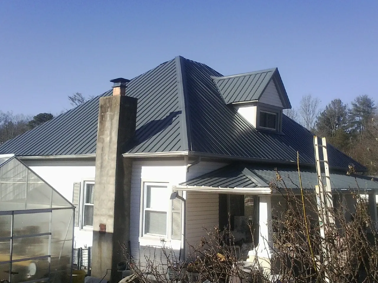 Dark blue standing seam metal roof on a white farmhouse with dormer — Slate & Tile Roof Repair by Roofing Brothers in Vandiver
