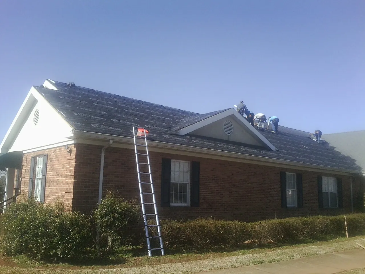 Crew tearing shingles off a brick ranch roof with a ladder set — Emergency Roof Repair work by our crew in Vandiver