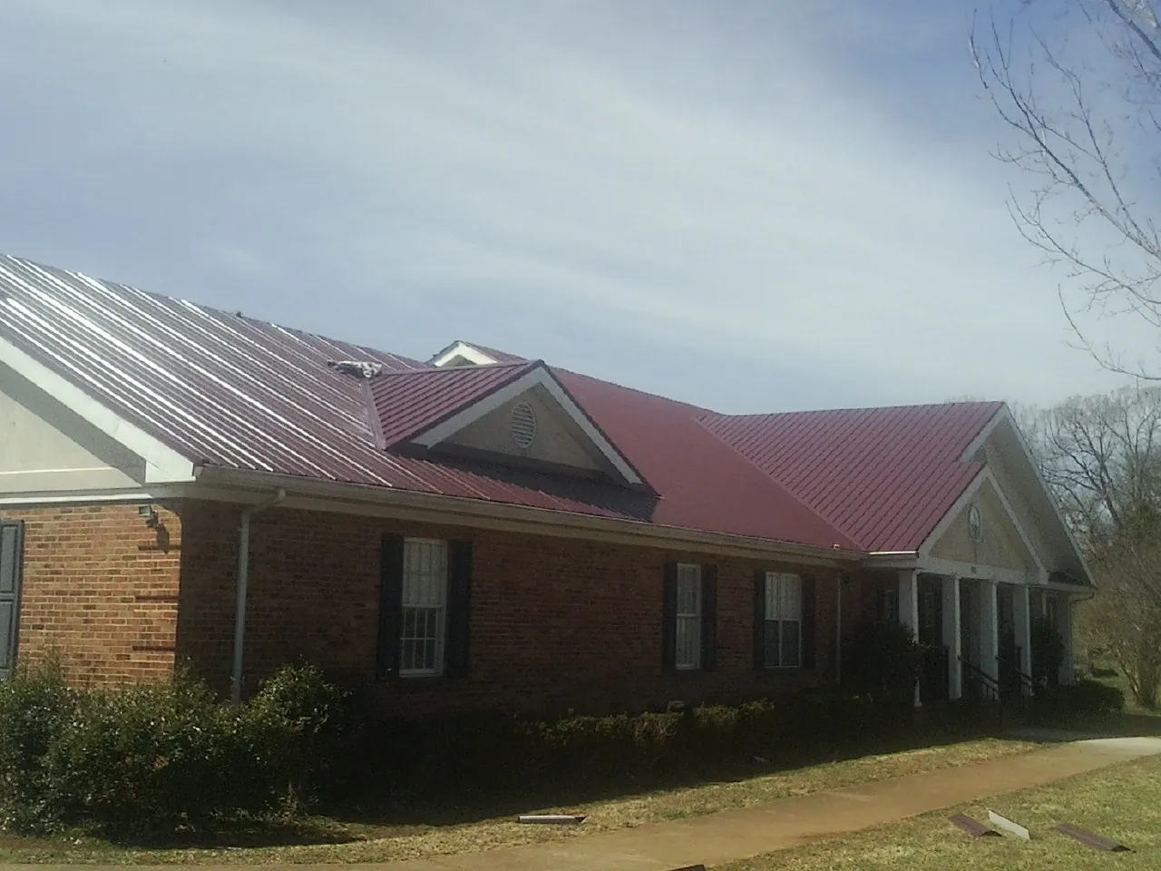 Red metal roof with gabled entries on a long brick building, from a Hail Damage Roof Repair job in Vandiver