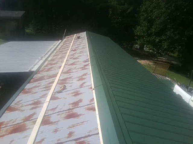 Old rusted panels beside newly installed green metal roofing — Wind Damage Roof Repair by Roofing Brothers in Vandiver