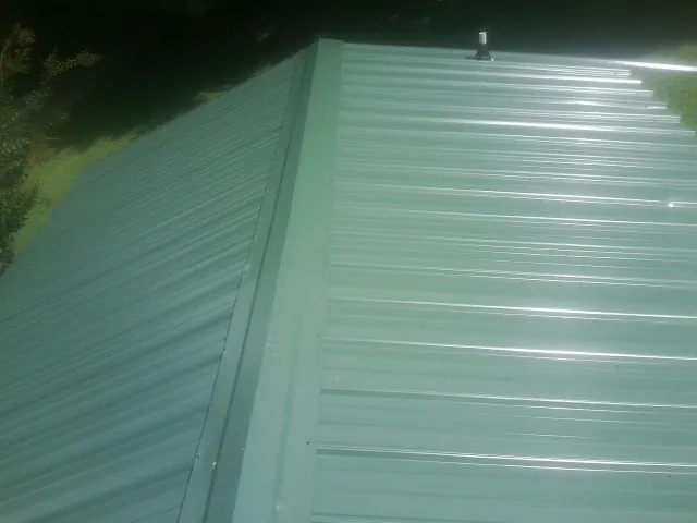 New green metal panels meeting at the ridge of a roof — Flat Roof Repair work by our crew in Vandiver