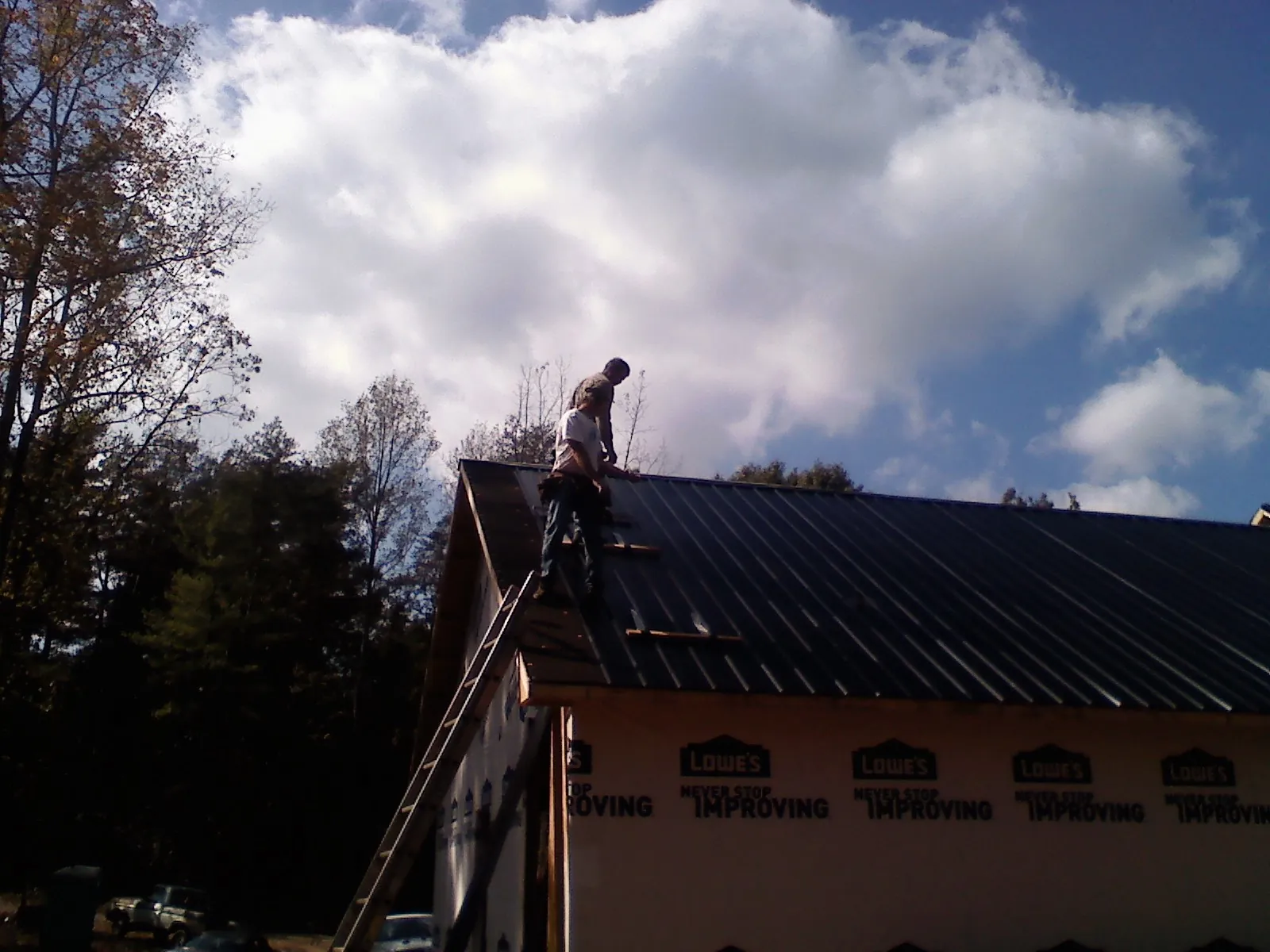 Roofer fastening dark metal panels high against a cloudy sky, from a Roof Inspection job in Vandiver