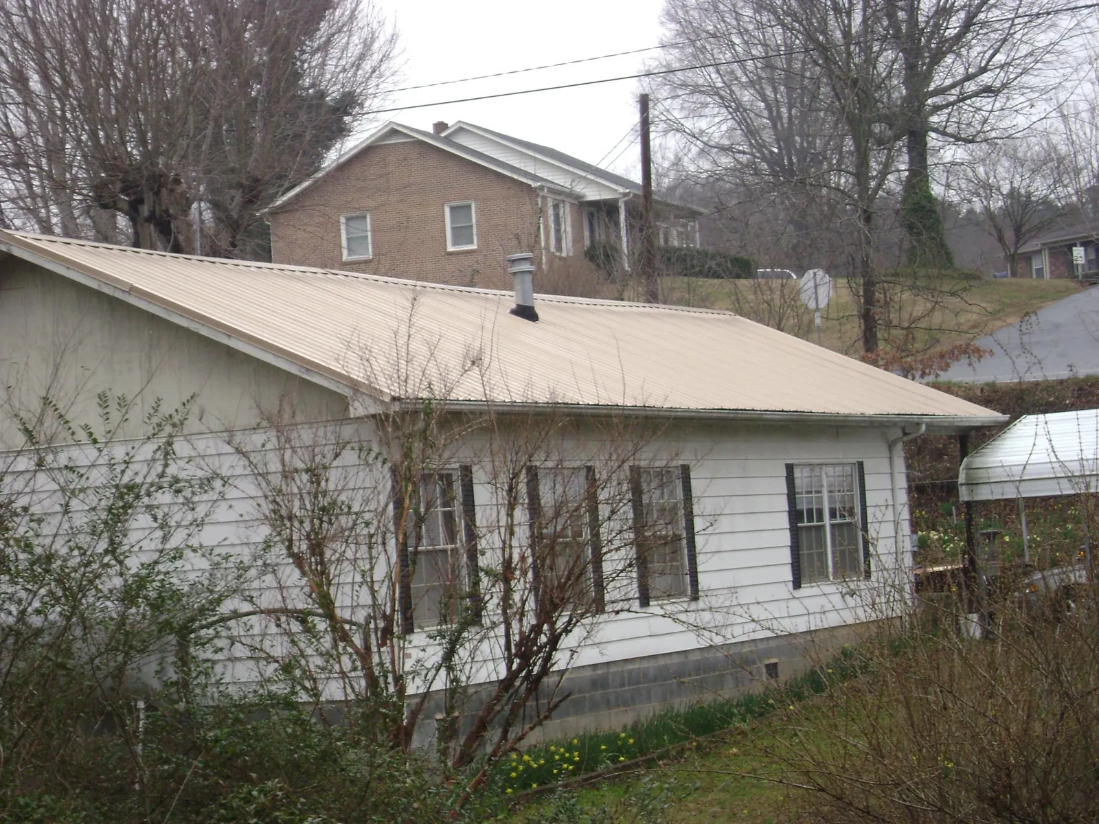 Tan metal roof on a white sided house set into a hillside — Commercial Roofing by Roofing Brothers in Vandiver